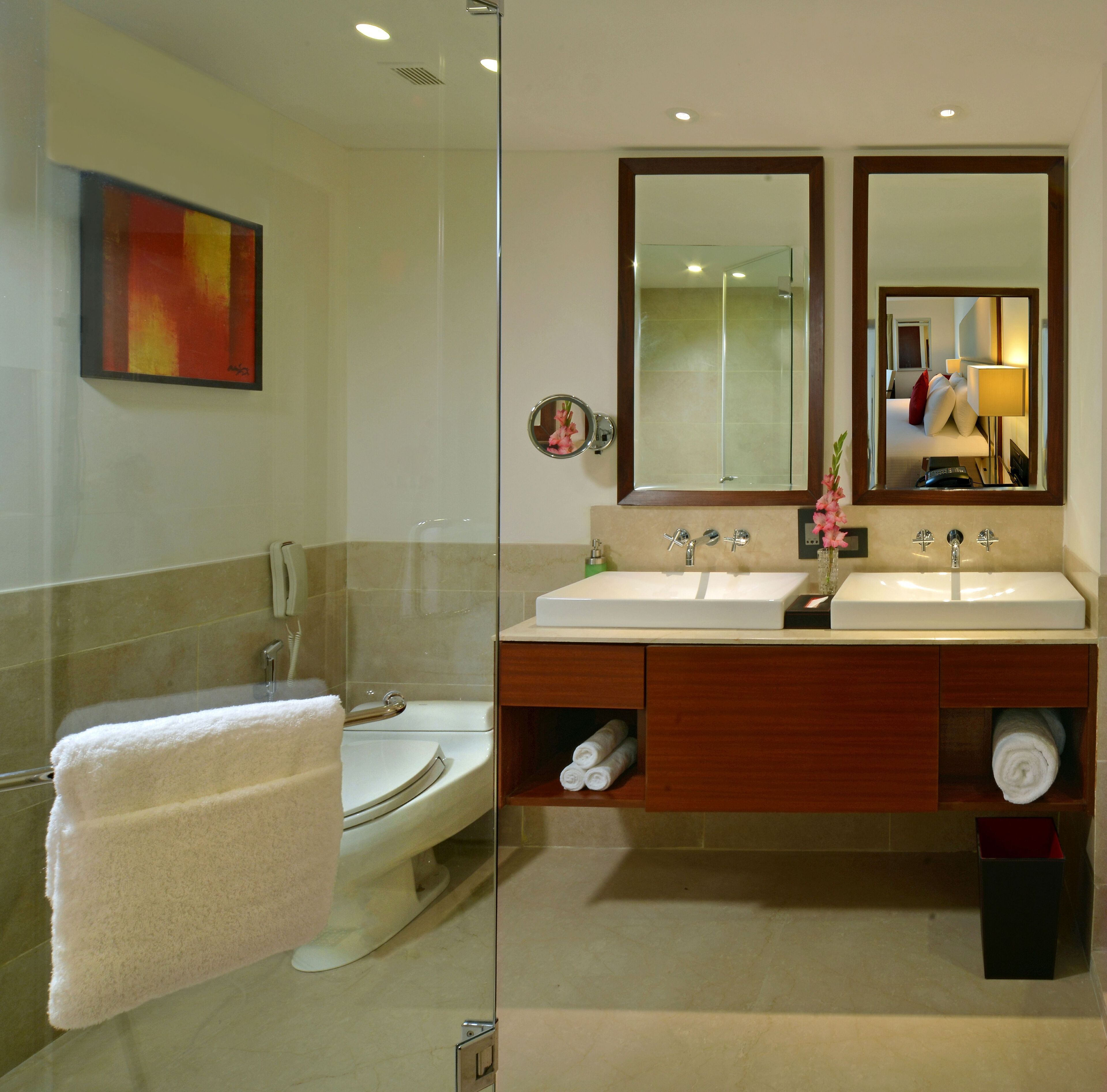 A modern bathroom with a glass shower enclosure, a toilet, a double sink vanity with a mirror, and a towel rack.