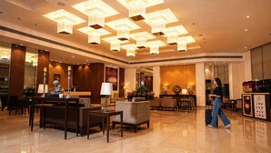 A spacious lobby with a high ceiling, multiple chandeliers, a reception desk, and comfortable seating areas.