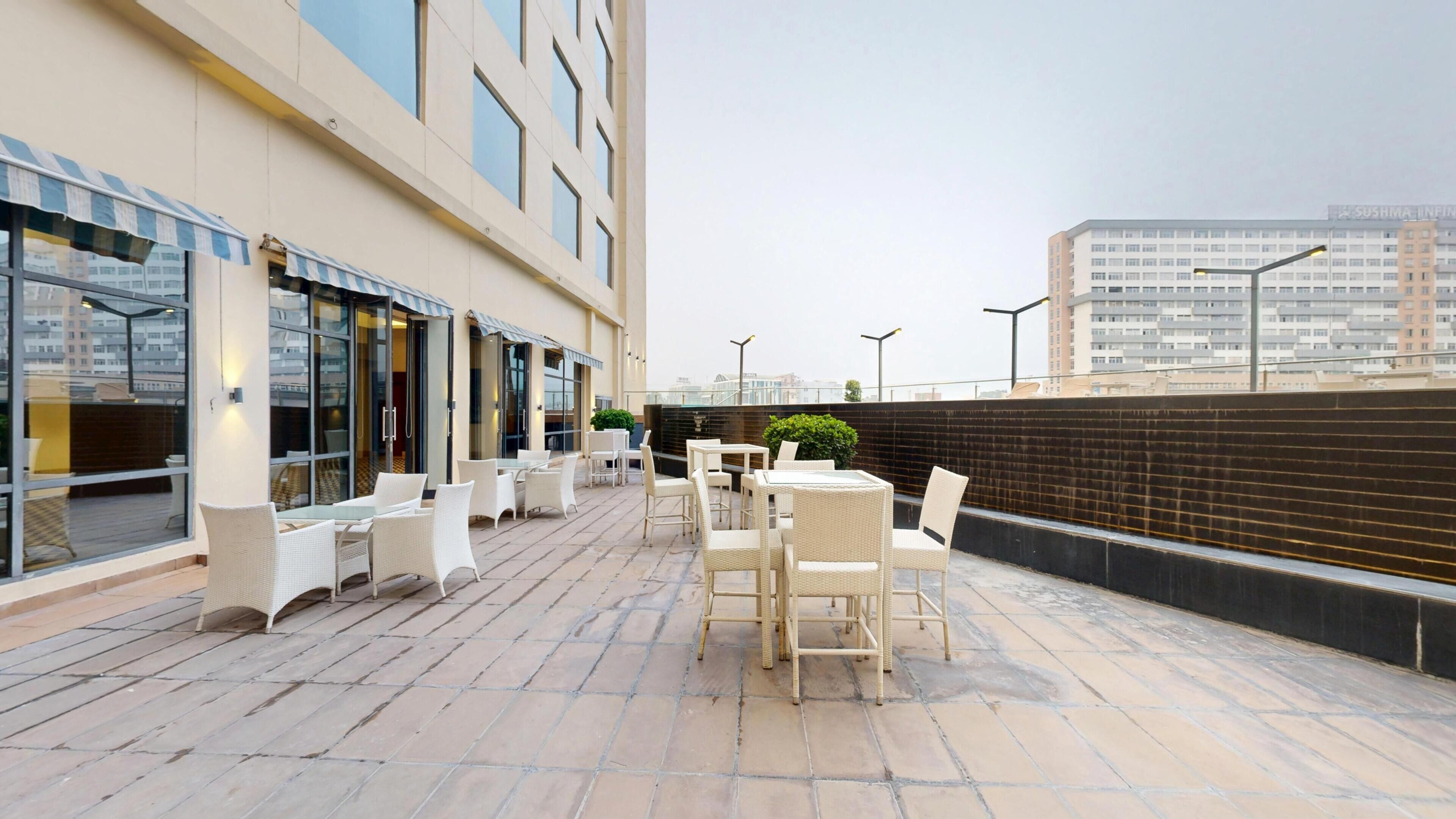 Une terrasse sur le toit avec des sièges extérieurs, une vue sur la ville et un bâtiment doté de grandes fenêtres.