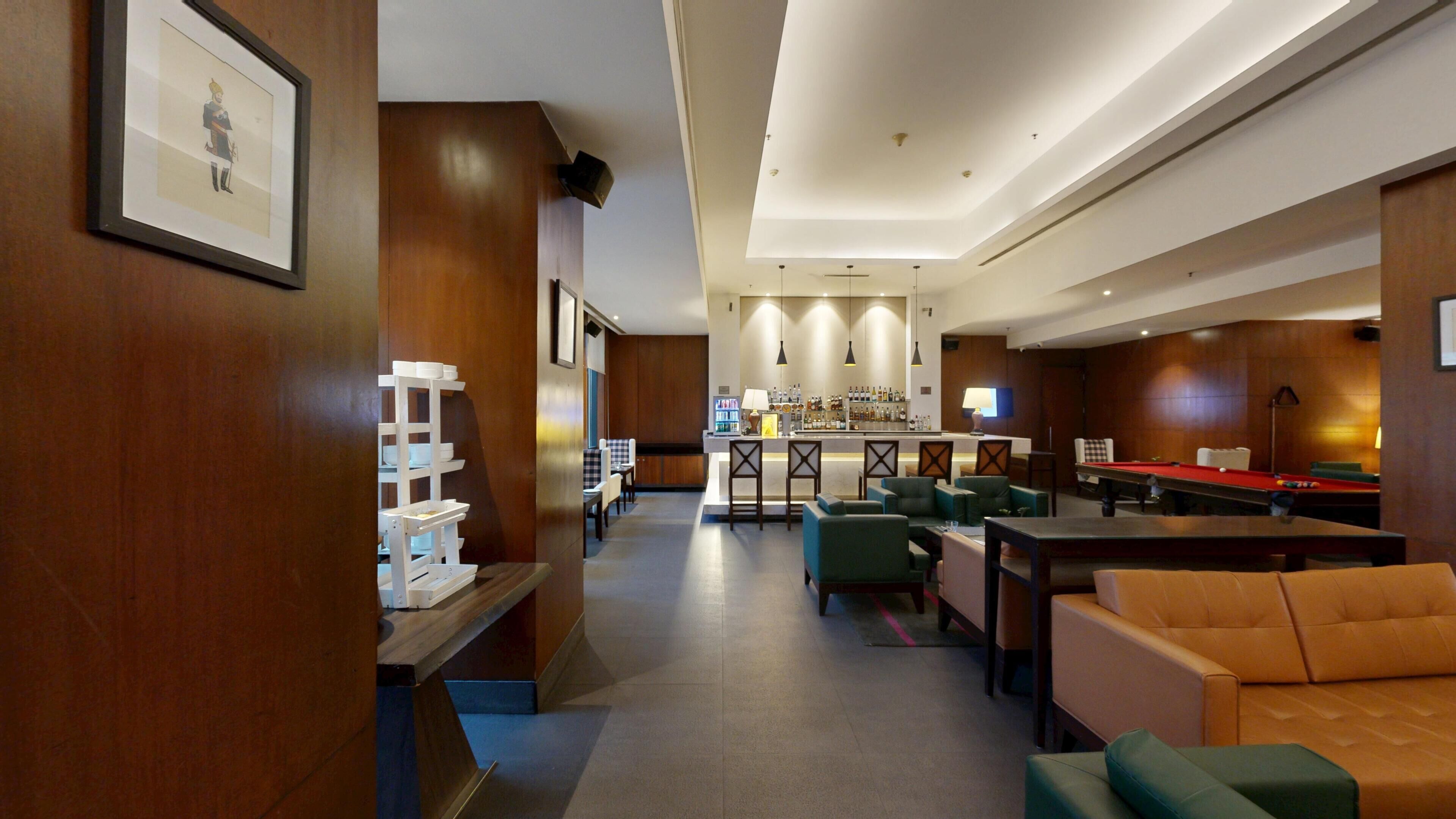 Um saguão de hotel com mesa de bilhar, área de estar, bar e um quadro na parede.