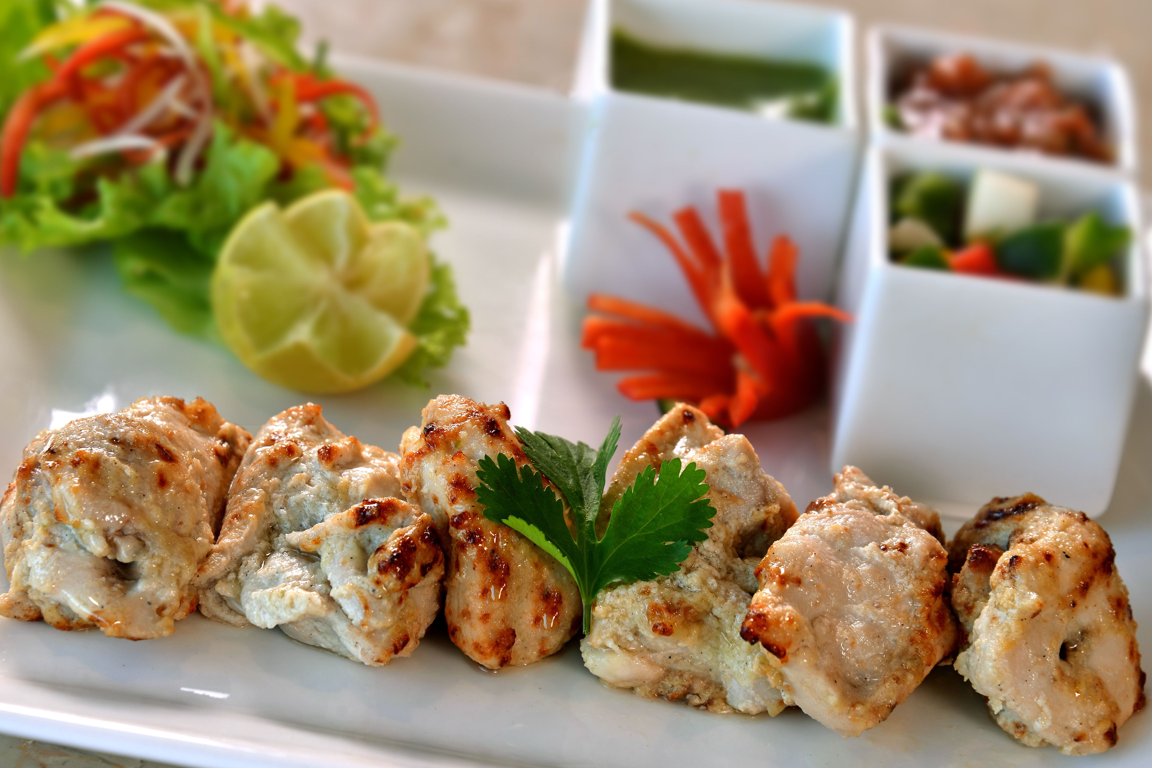 A plate of grilled chicken with a garnish, accompanied by a salad and a lime wedge.
