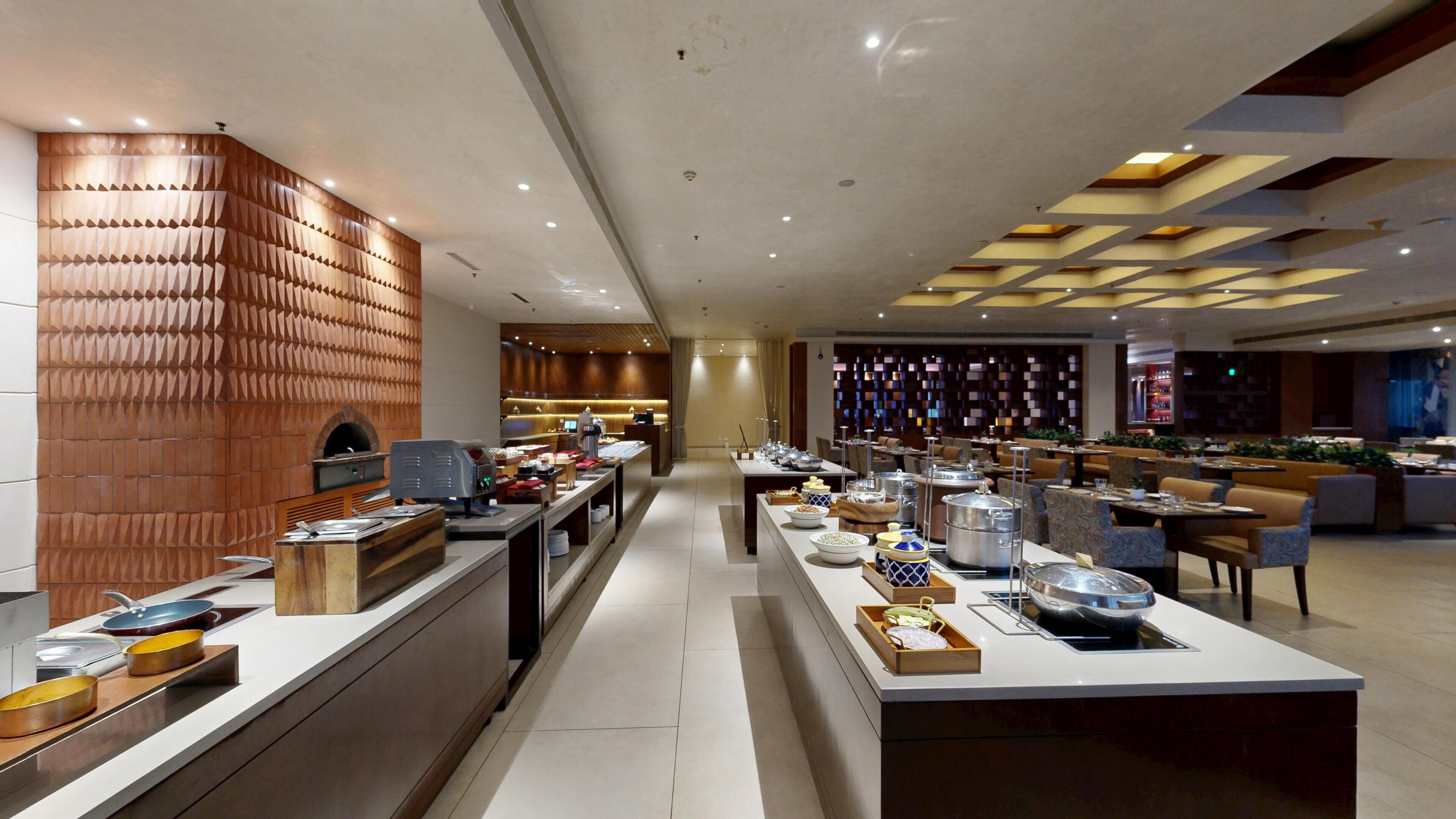 A modern restaurant with a long counter, multiple tables, and a decorative wall with geometric patterns.