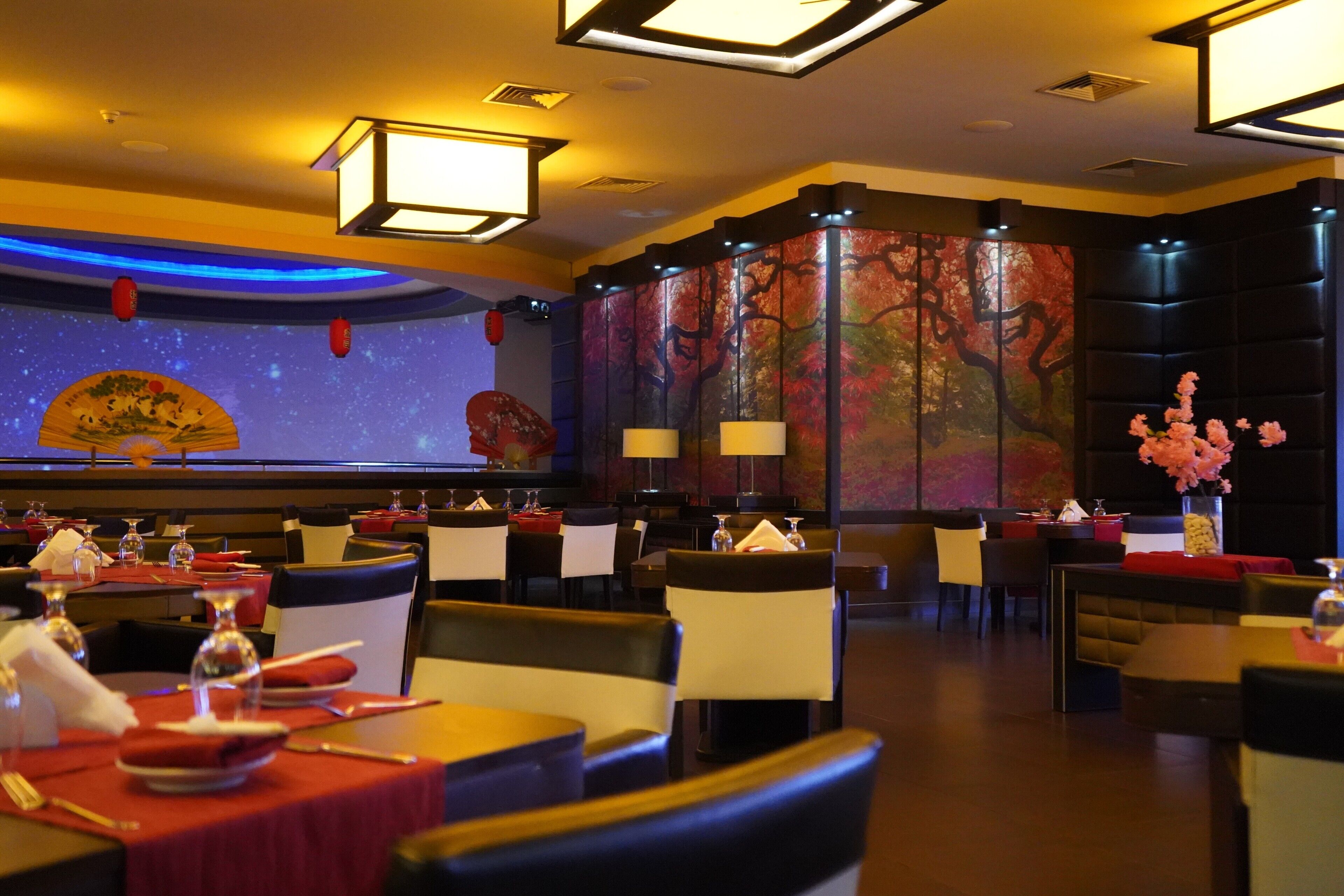 A restaurant with tables set for dining, a large decorative screen, and a wall with a tree painting.