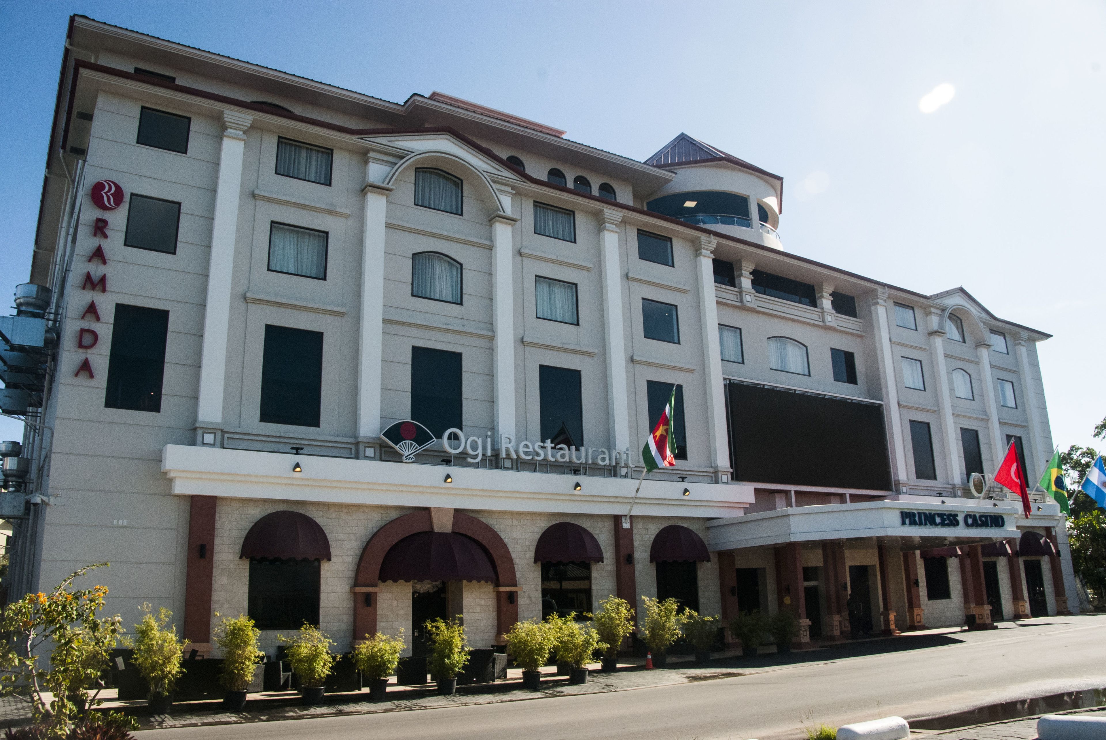 Ein mehrstöckiges Hotel mit einem auffälligen Schild mit der Aufschrift "Princess Casino", dem Logo "Ramada" und einem Schild mit der Bezeichnung "Ogi Restaurant".