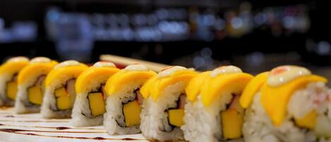 Una hilera de rollos de sushi con cobertura amarilla, dispuestos sobre un plato blanco con salpicaduras de salsa.