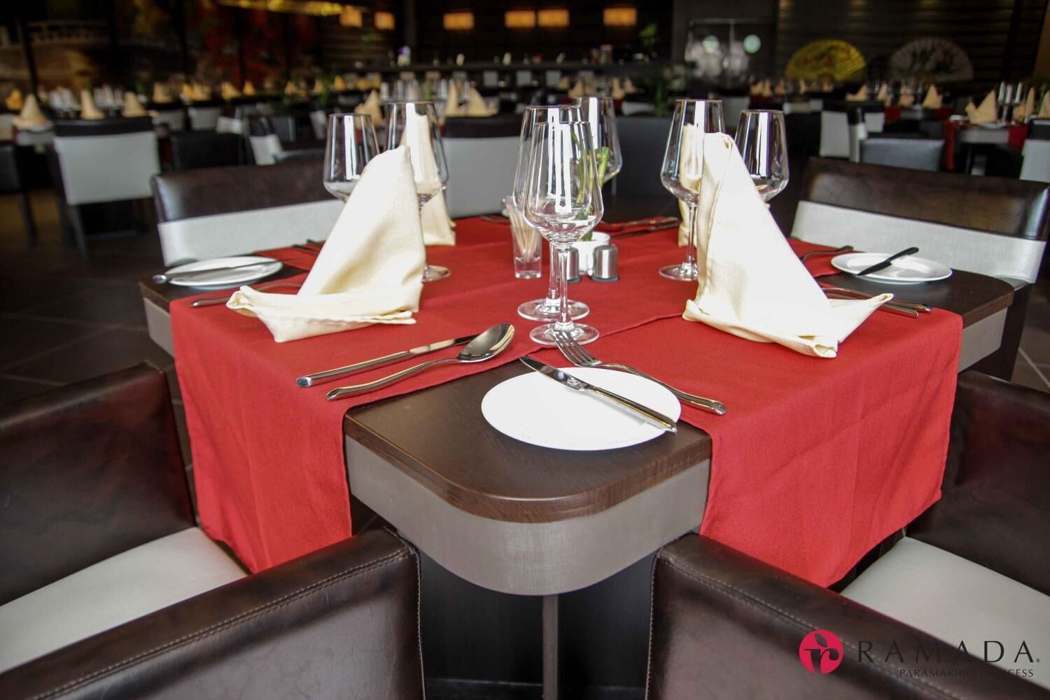 A restaurant setting with a red tablecloth, neatly set dining table with silverware and plates, and a logo in the bottom right corner.
