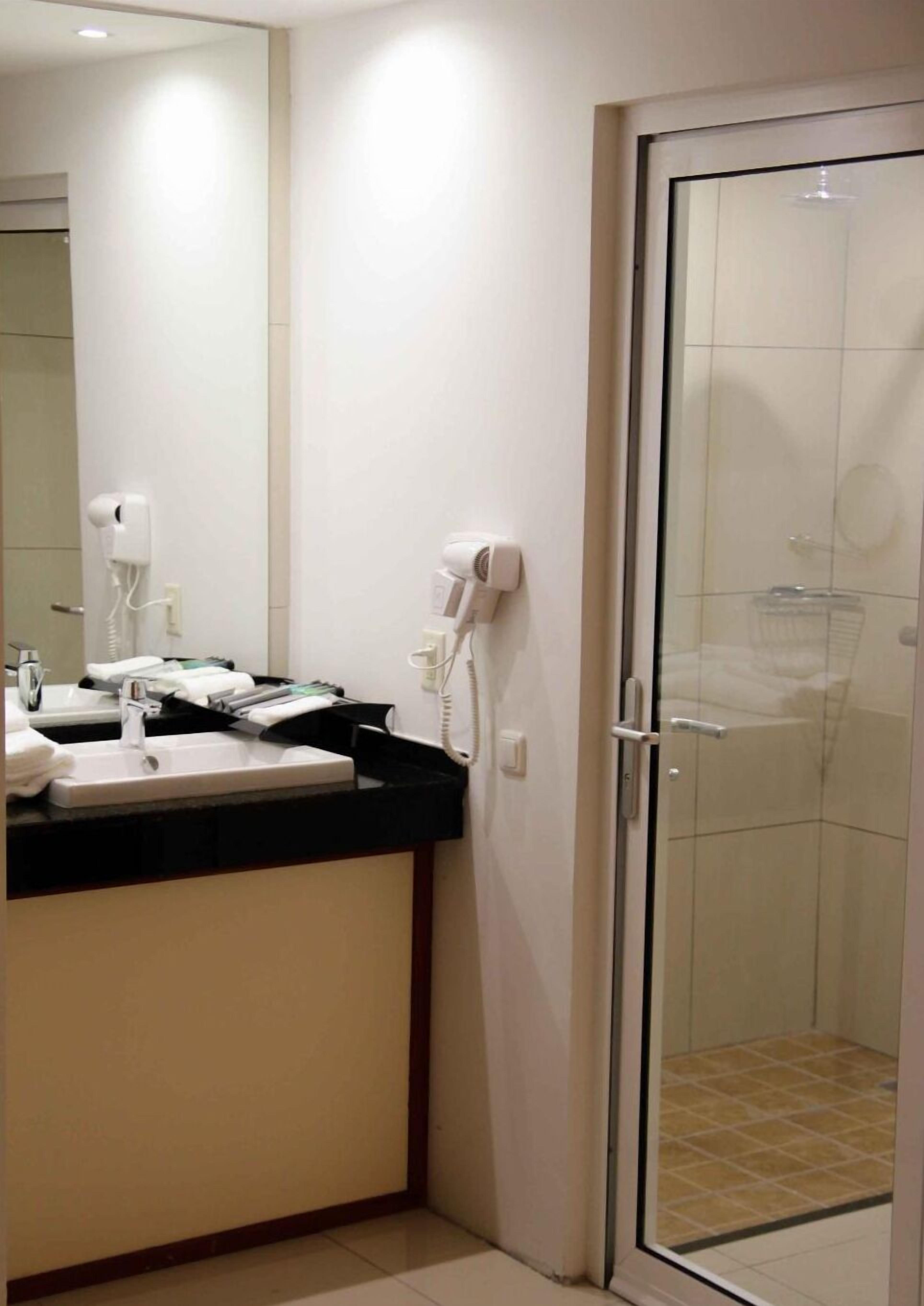A bathroom with a sink, mirror, hairdryer, and a glass shower door.