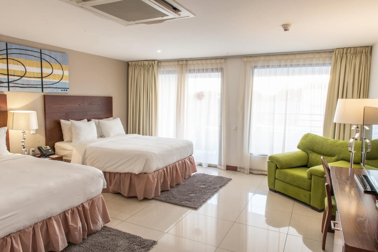 Una habitació d'hotel amb dos llits, una butaca verda, un escriptori de fusta i un quadre al mur.
