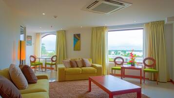 A bright living room with a yellow sofa, a wooden coffee table, and a dining area with green chairs.