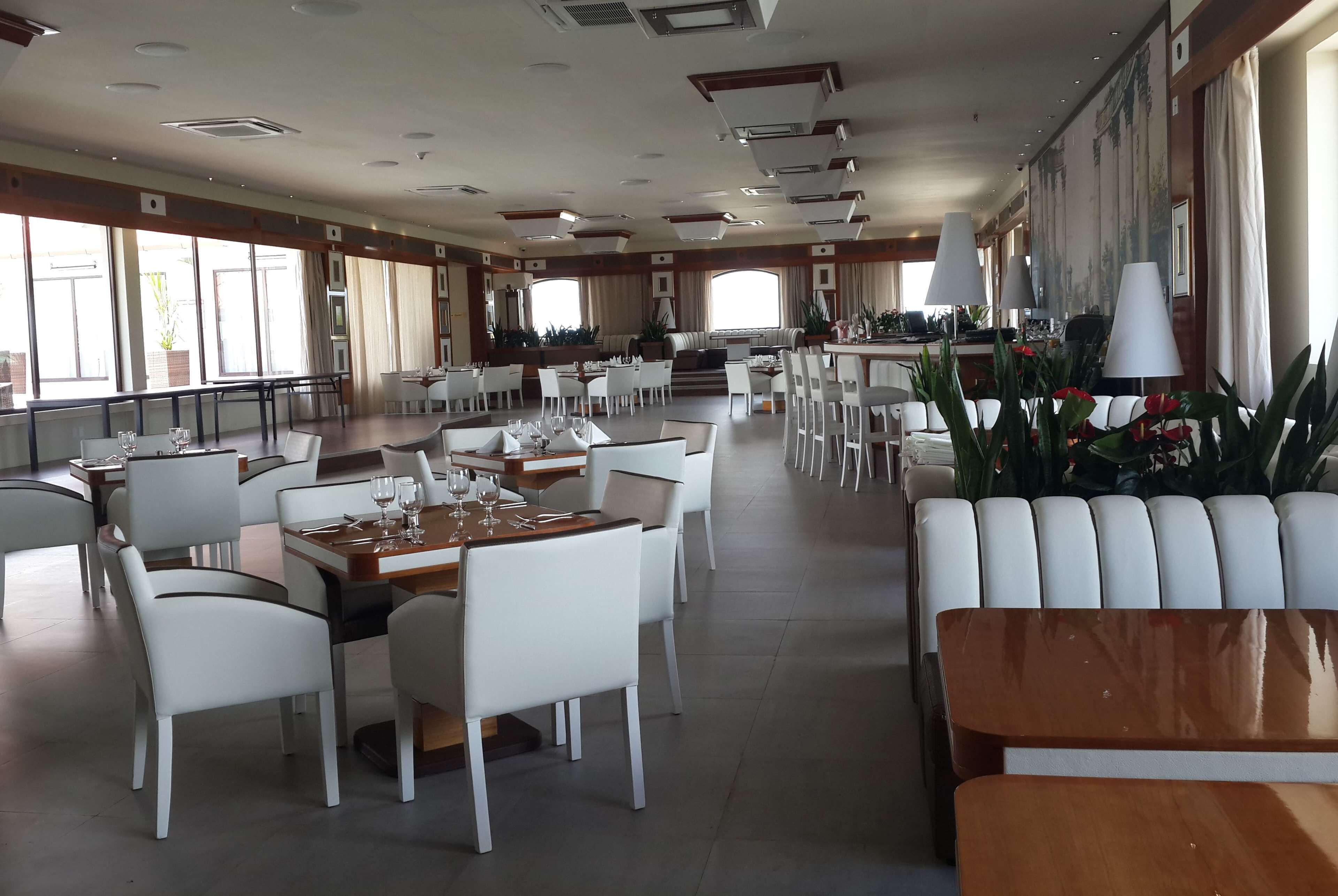 Un restaurant spacieux avec de hauts plafonds, de grandes fenêtres et des meubles blancs.