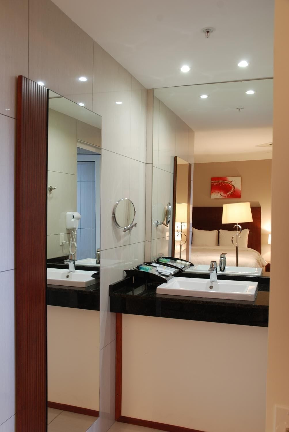 A hotel bathroom with two sinks, a mirror, and a shower.