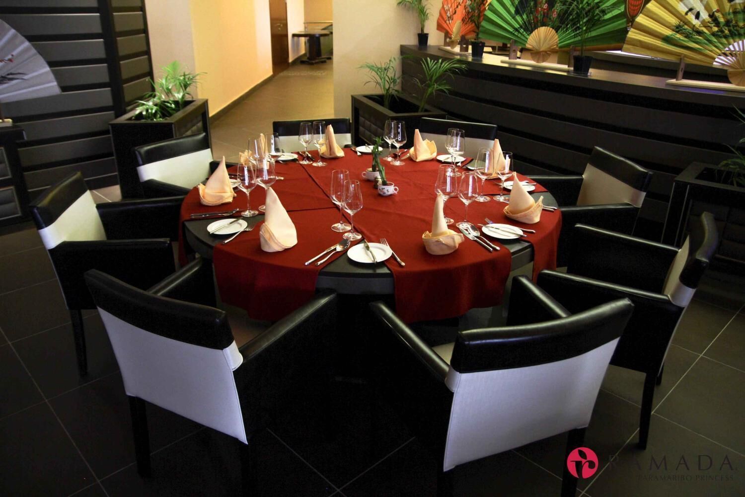 Une table ronde recouverte d’une nappe rouge, entourée de chaises noires avec des coussins blancs.