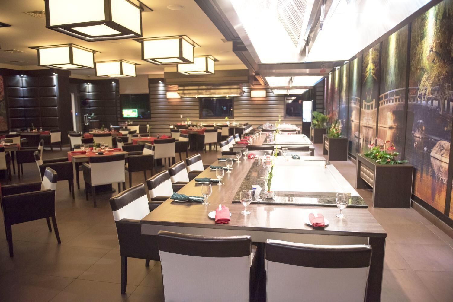 Een ruim restaurant met lange gedeelde tafels, zwart-witte stoelen en moderne hanglampen.