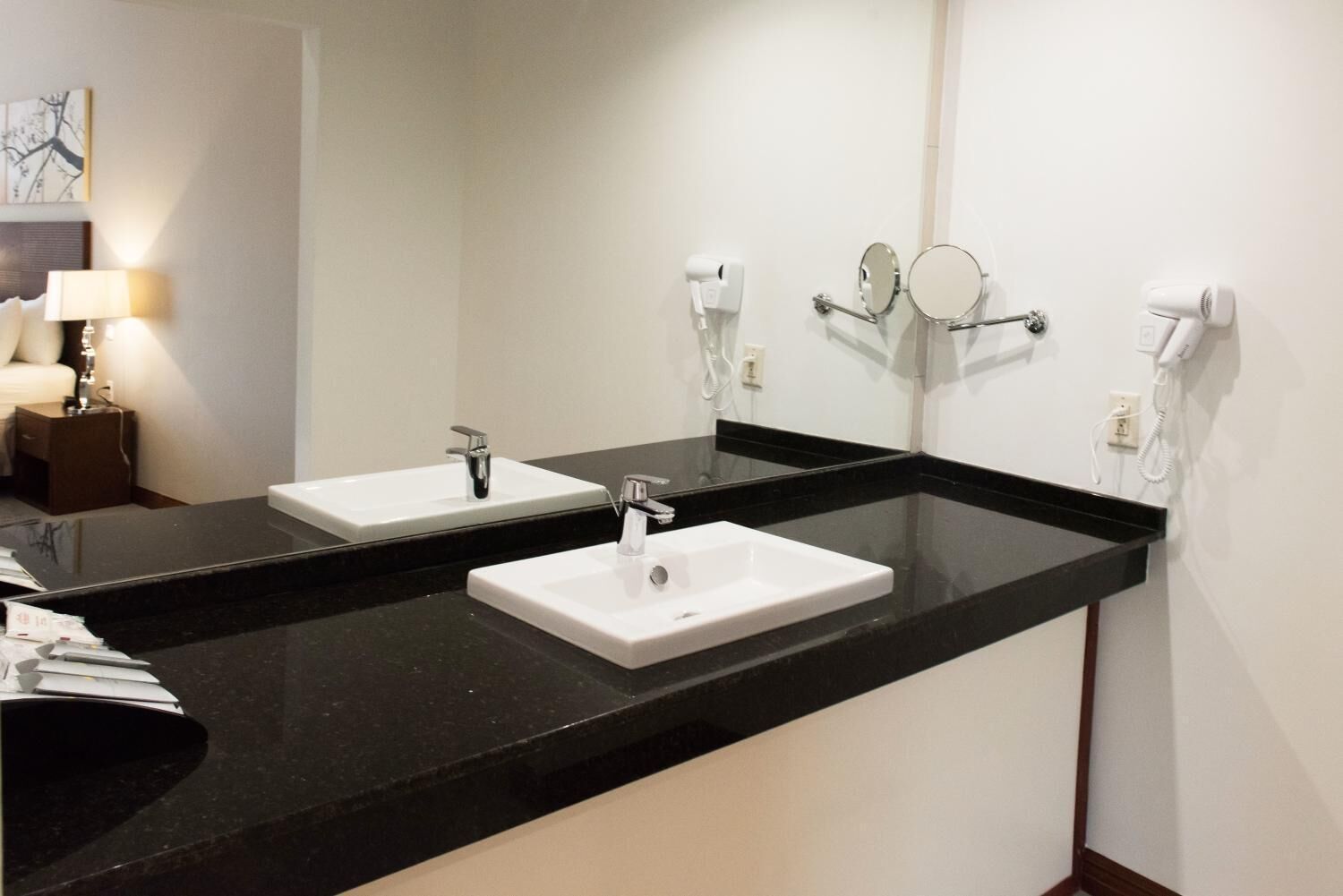 Un baño de hotel con dos lavamanos, un espejo grande y un secador de pelo en la pared.