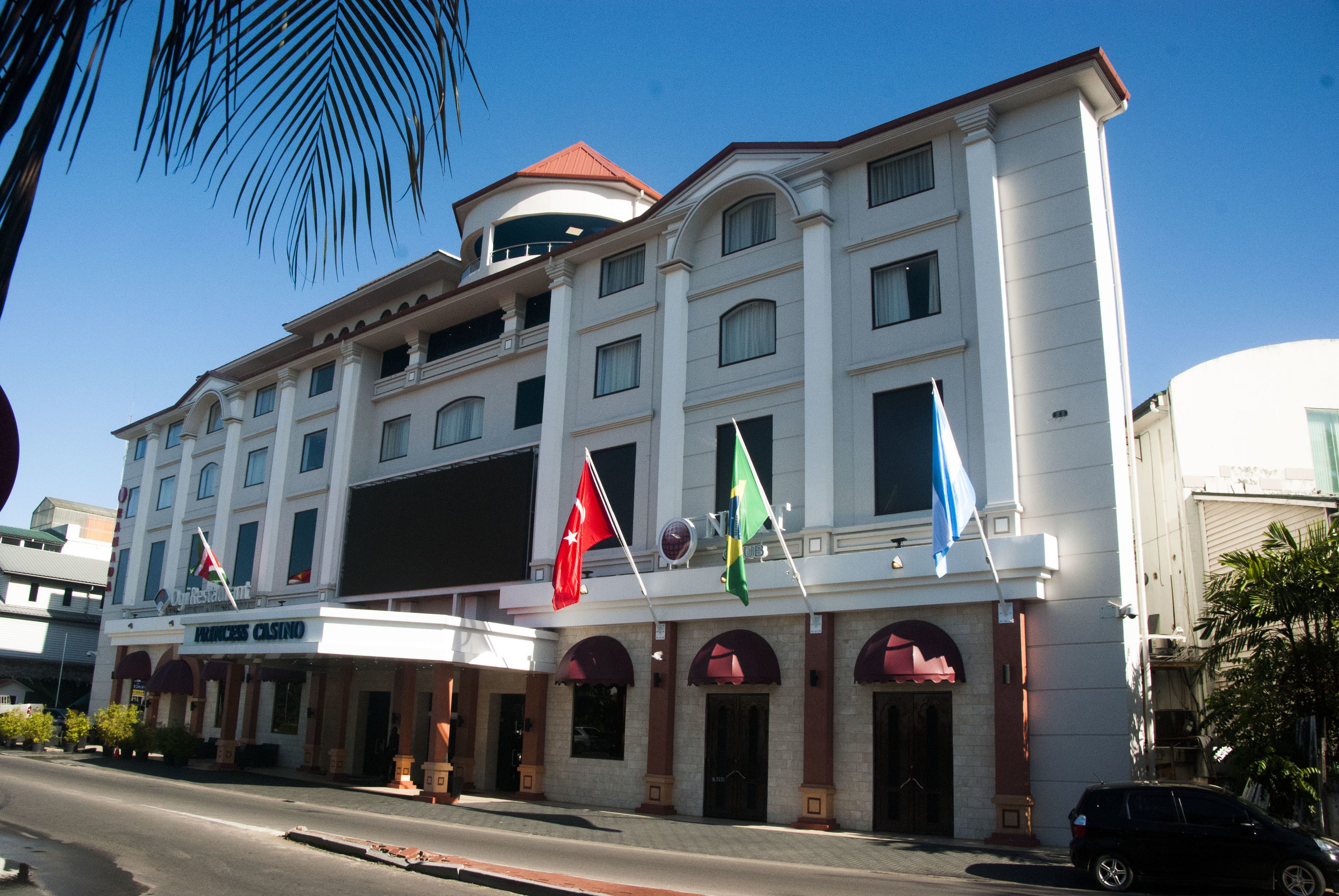 A multi-story hotel with a white facade, arched windows, and a red roof. Flags are displayed on the building's facade.