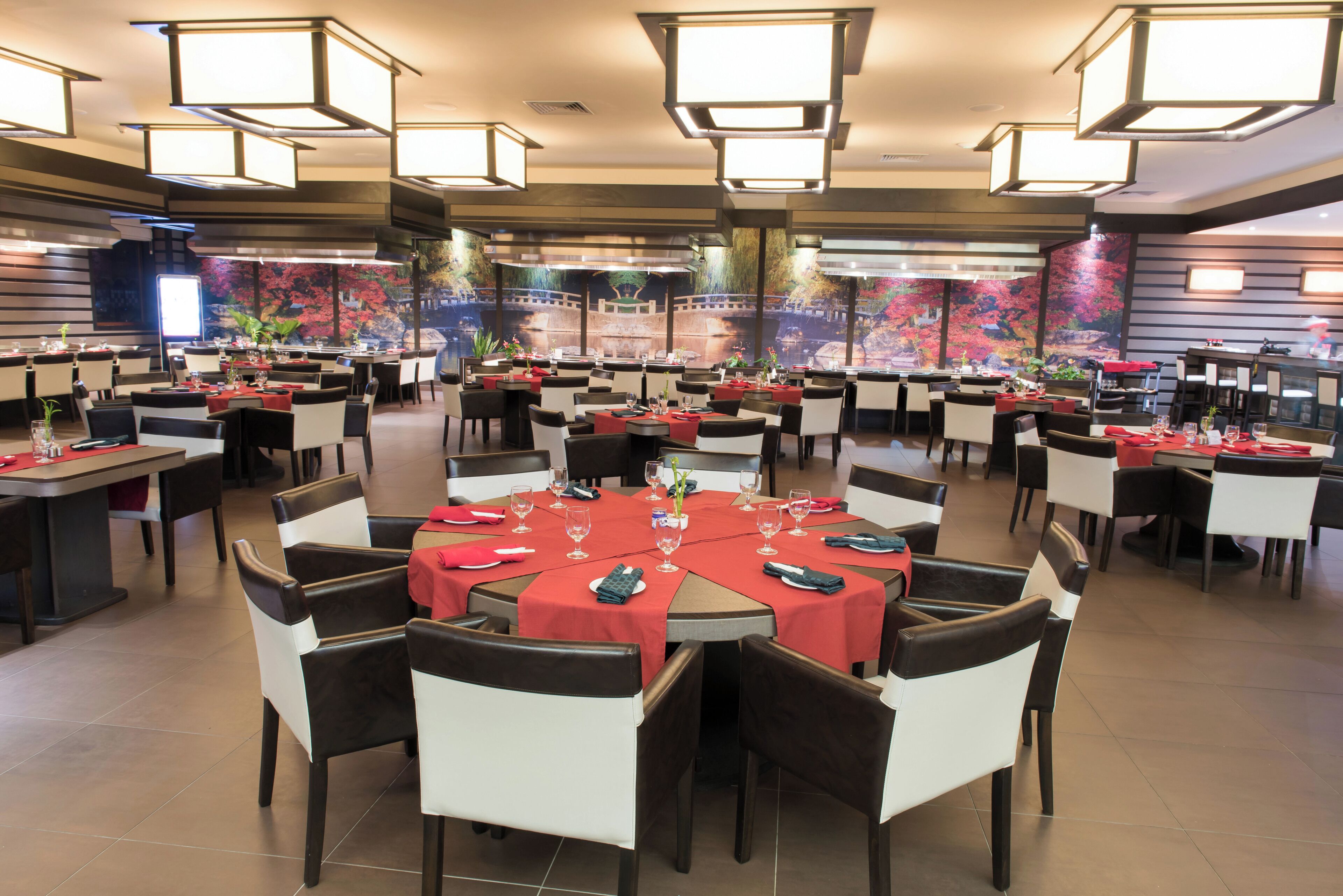 Un comedor amplio con varias mesas redondas, cada una dispuesta con sillas y manteles rojos.