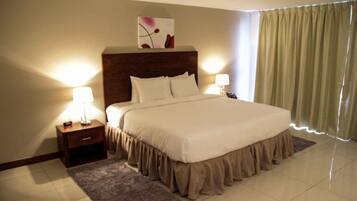 A neatly made bed with a headboard, bedside lamps, a small bedside table, and a window with curtains.