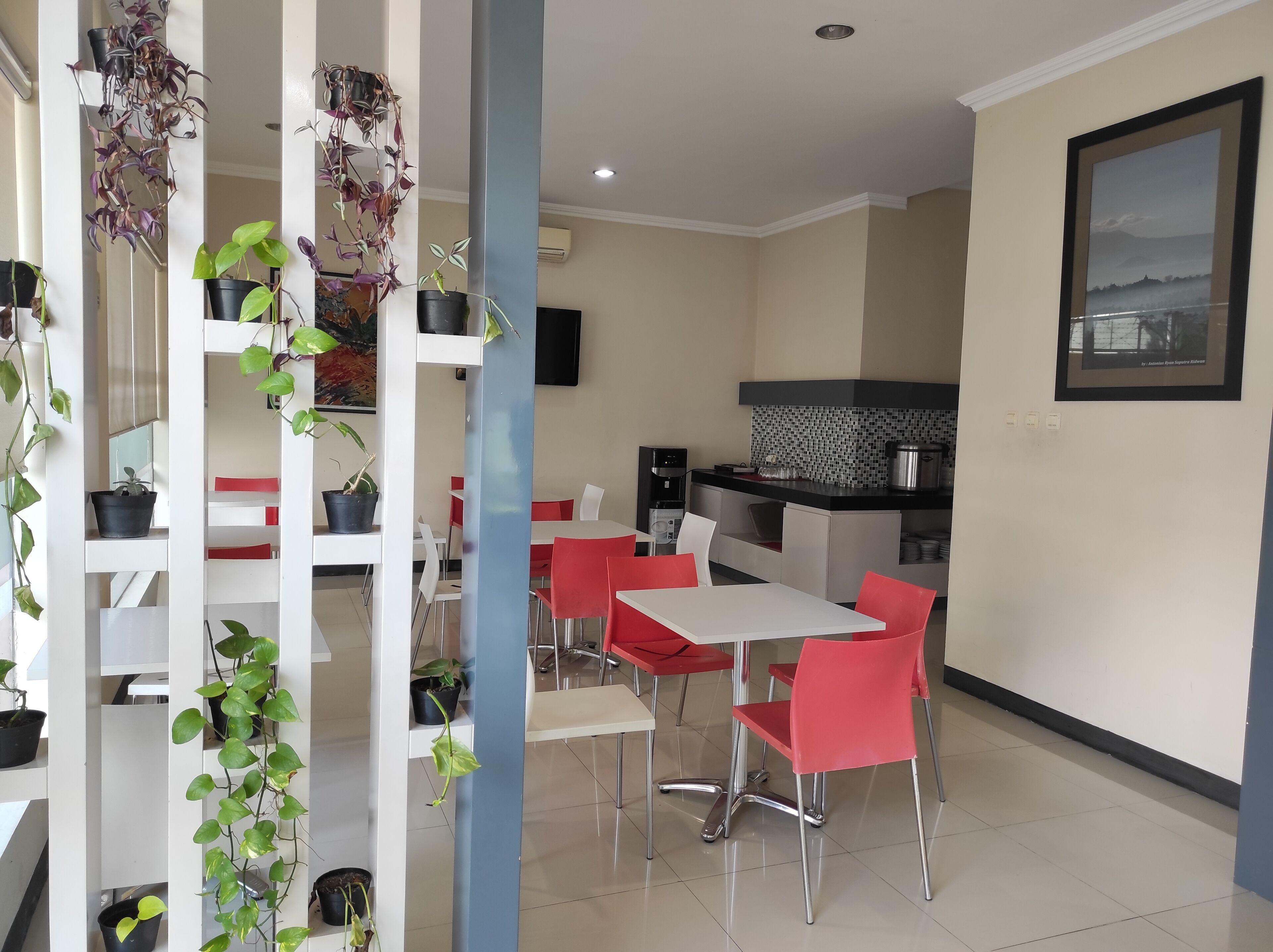 Cocina moderna con encimera negra, armarios blancos y salpicadero de azulejos. Hay una zona de comedor con una mesa blanca y sillas rojas.