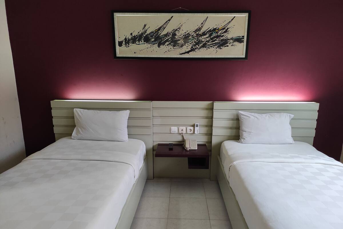 A hotel room with two beds, a nightstand with a phone, and a framed abstract painting on the wall.