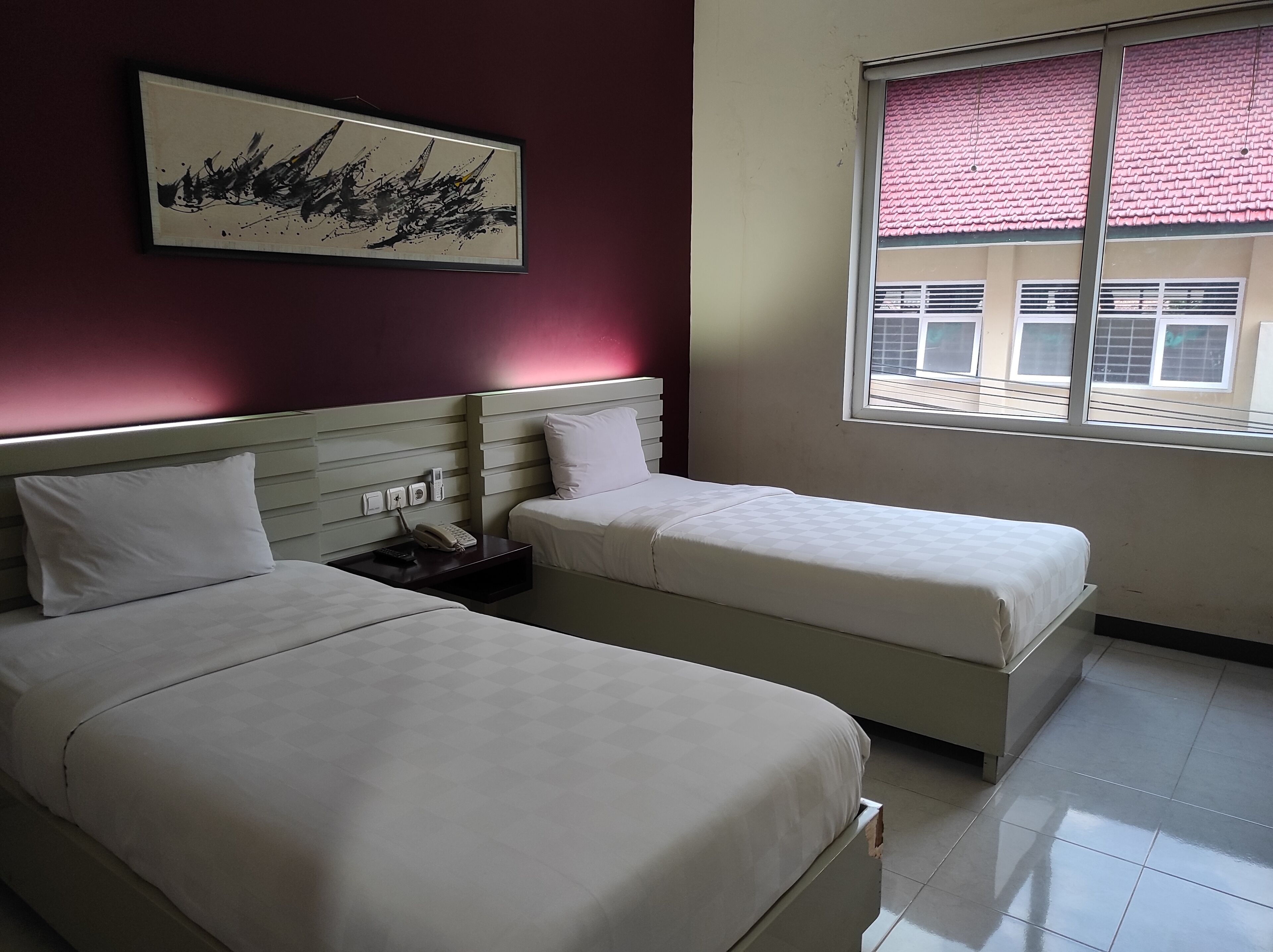 Une chambre d’hôtel avec deux lits, une table de chevet avec un téléphone et une fenêtre donnant sur des immeubles.