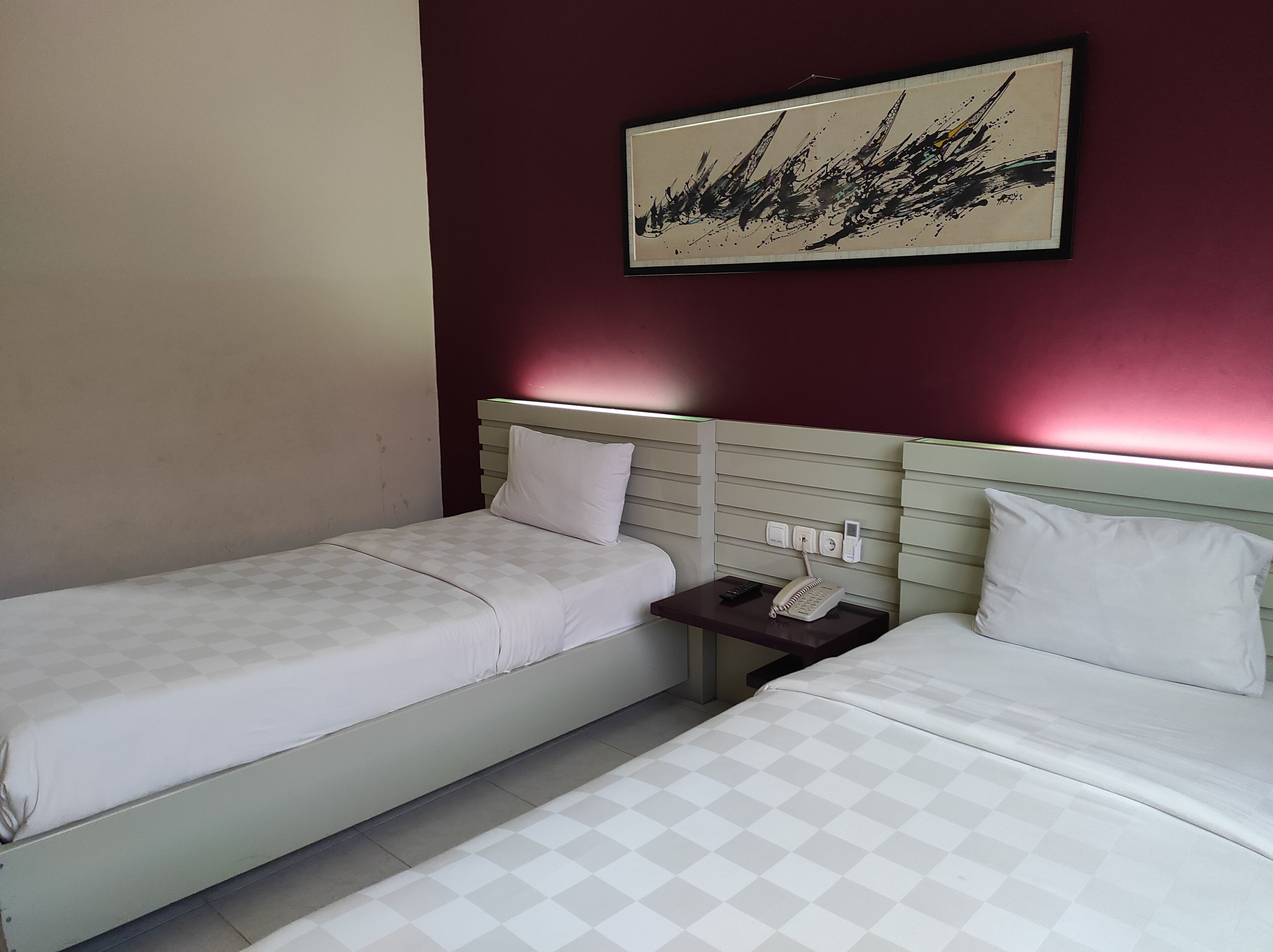Habitació d'hotel amb dos llits individuals, una tauleta de nit amb telèfon i comandament a distància, i una obra d'art penjada a la paret.