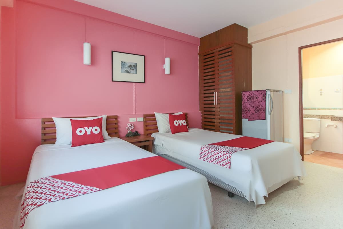 Ein Hotelzimmer mit zwei Betten, rosa Wänden, einem Holzschrank, einem Kühlschrank und einem durchgegangenen Badezimmer.