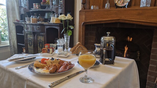 A breakfast table with eggs, bacon, toast, and juice, set in front of a fireplace with a decorative mirror and a vase of flowers. - The Sycamore Guest House (York)