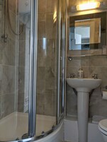 Un baño con ducha de vidrio, lavamanos pedestal y espejo sobre él.