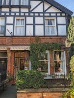 A two-story Tudor-style building with a brick facade, white and black timber framing, and a black iron fence.