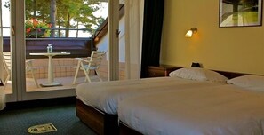 A hotel room with a bed, a small table, and a chair. There is a balcony with a view of trees and flowers. - Golf Hotel La Pinetina (Carbonate)