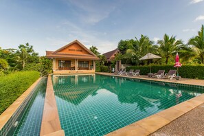 Una piscina con sillones reclinables y una casa al fondo.