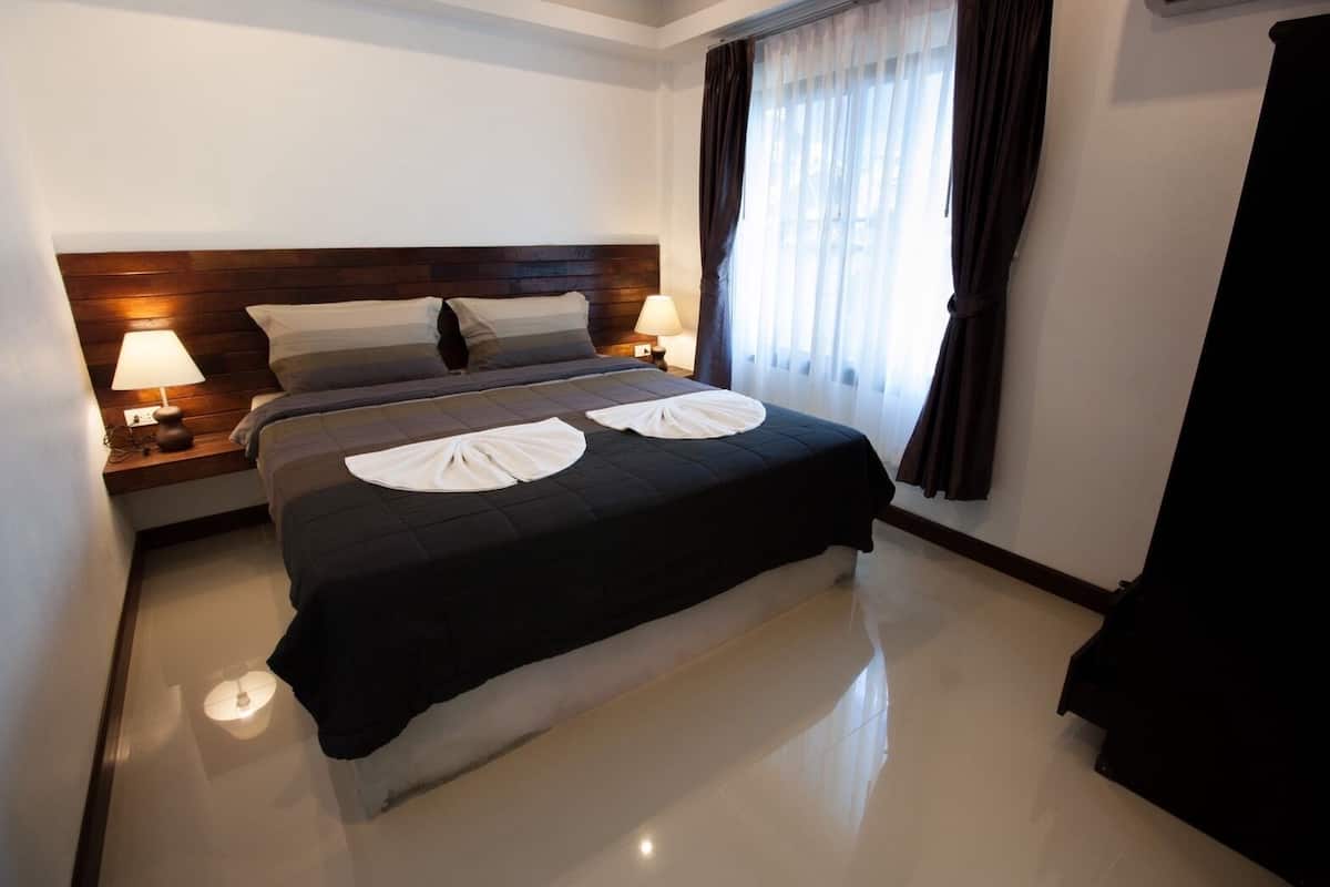 A hotel room with a large bed, two bedside lamps, a wooden headboard, a window with curtains, and a black curtain on the right.