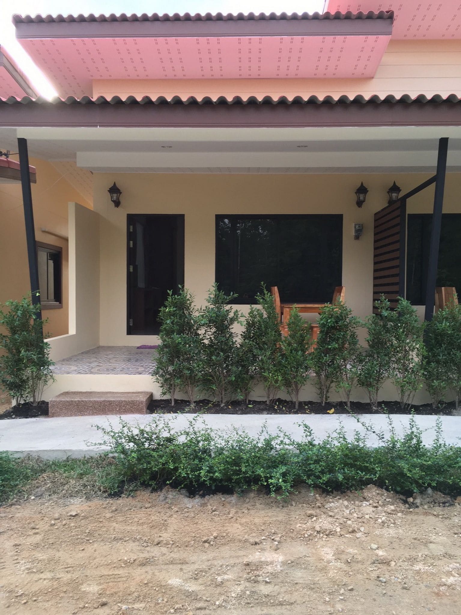 A house with a covered porch, a small garden, and a dirt driveway.