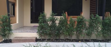 Una casa con porche cubierto, un pequeño jardín y un camino de tierra.
