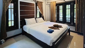 Een moderne hotelkamer met een groot bed, een houten hoofdbord en grote ramen met gordijnen.