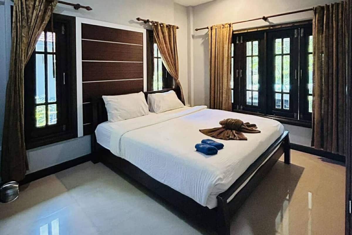 A modern hotel room with a large bed, a wooden headboard, and large windows with curtains.