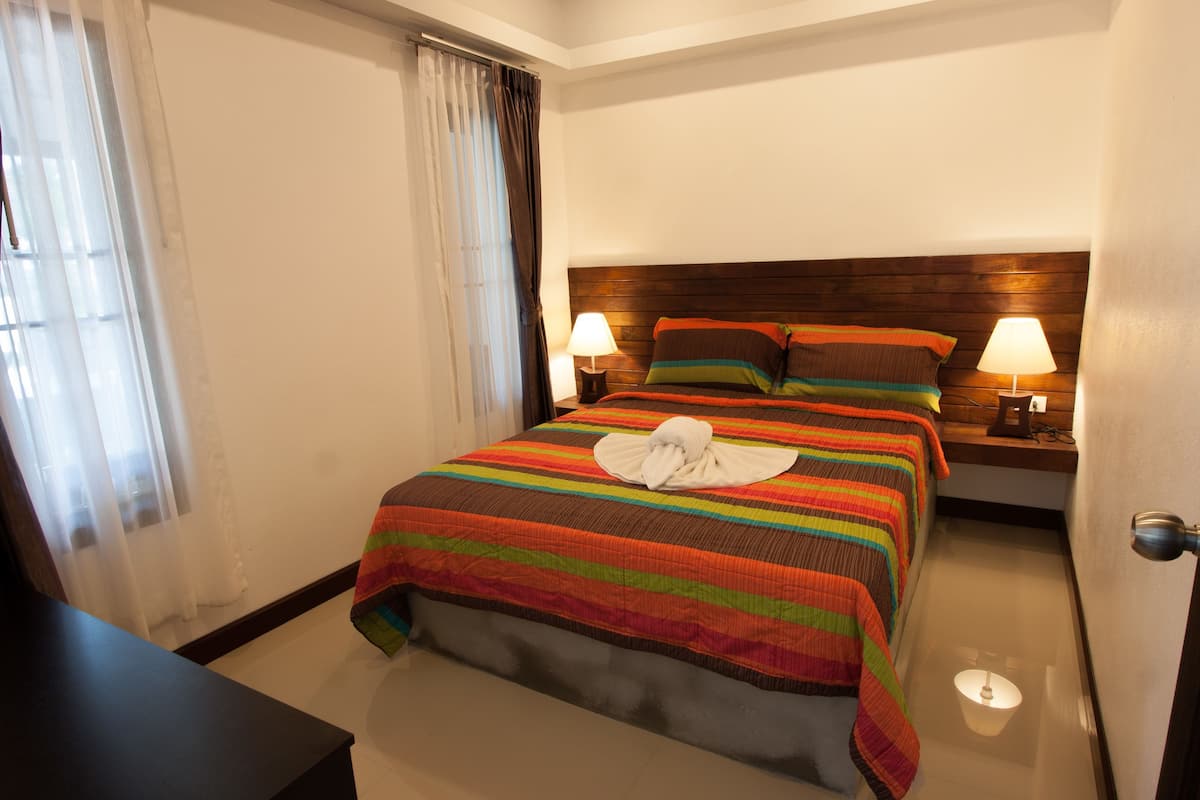 A neatly made bed with a striped bedspread and pillows, two bedside lamps, and a wooden headboard.