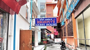 A narrow street with buildings on either side, a sign for a guest house, and a motorcycle parked on the right. - Highfive Guest House (Pattaya)