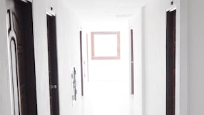 A bright, narrow hallway with white tiled floors and doors on both sides. - Highfive Guest House (Pattaya)