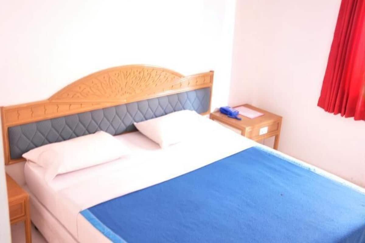 A bed with a headboard, a bedside table, and a red curtain.