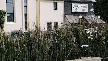 Un hotel llamado "Hotel Vert" con un diseño arquitectónico moderno, que presenta un letrero llamativo y una fuente al frente.