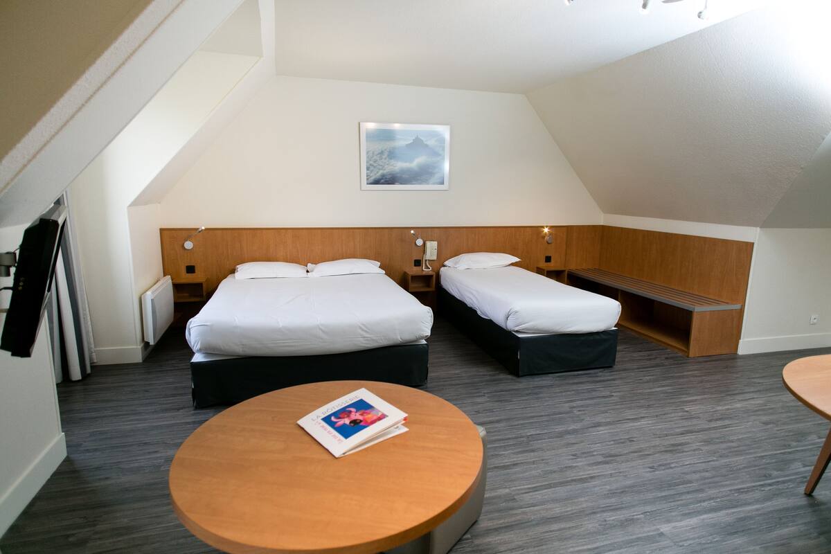 A hotel room with two beds, a round wooden table, and a framed picture on the wall.