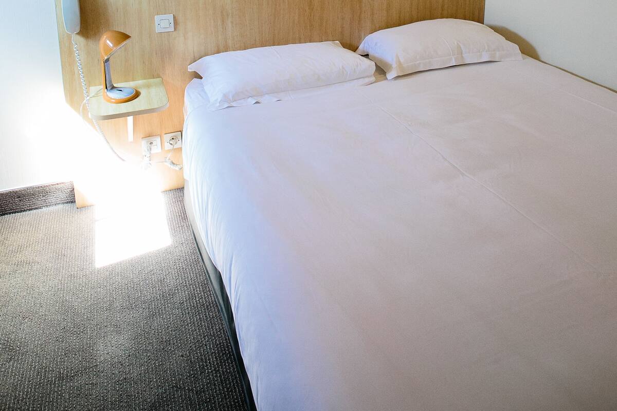 A hotel room with a bed, a nightstand, a lamp, and a painting on the wall.