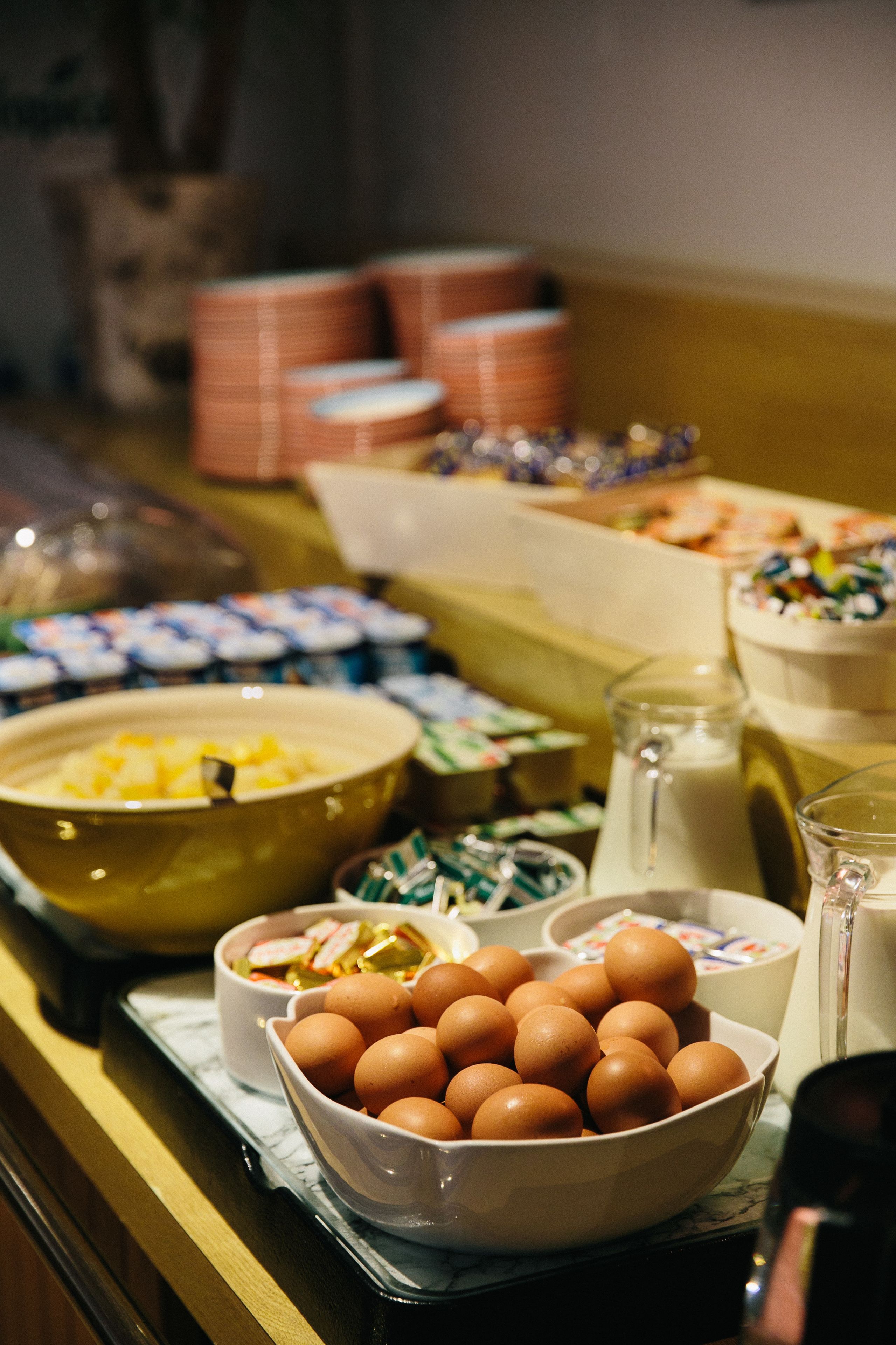 A buffet table with various food items including bowls of eggs, a pitcher of milk, and containers of condiments.