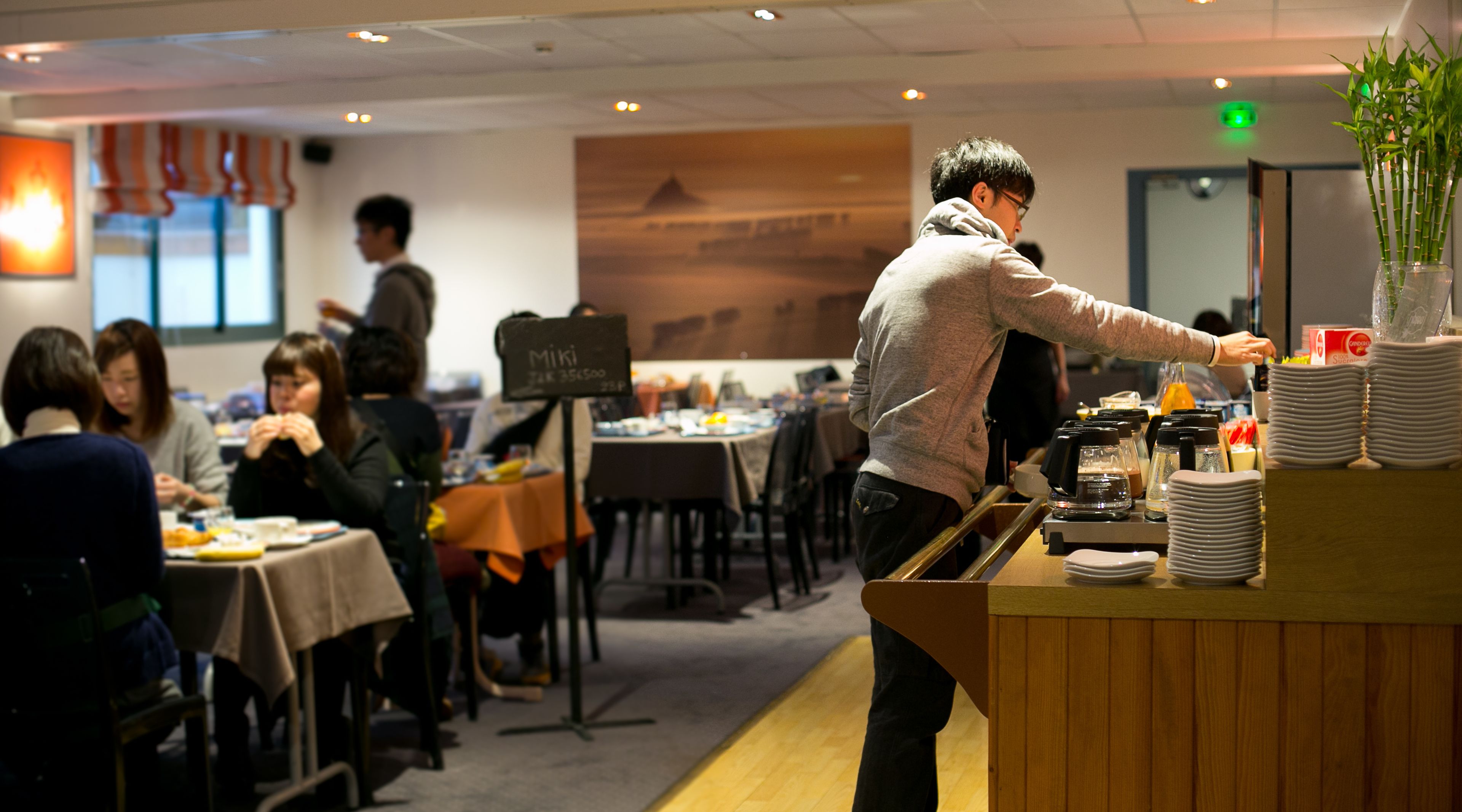 Un restaurant avec des tables et des chaises, un comptoir avec une machine à café et un tableau affichant le menu.
