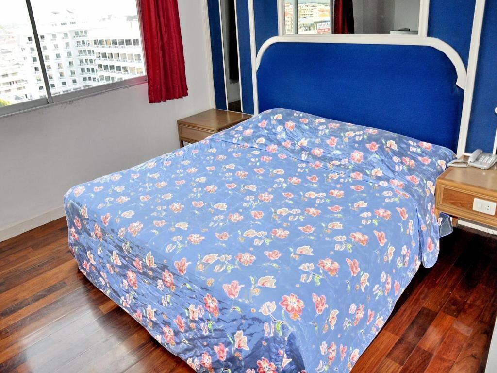 A bedroom with a bed, a wooden nightstand, a telephone, and a window with a view of buildings.