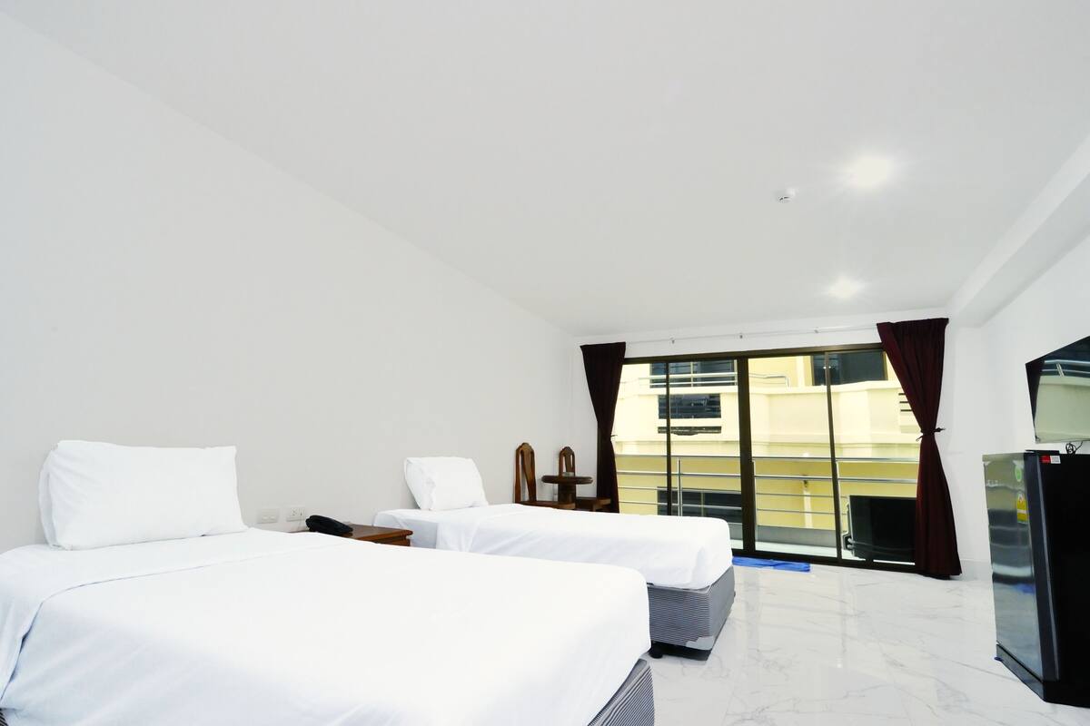 A hotel room with two beds, a desk, a chair, a window with curtains, and a refrigerator.