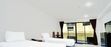 A hotel room with two beds, a desk, a chair, a window with curtains, and a refrigerator.