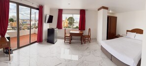 Une chambre d’hôtel avec un lit, un bureau et une chaise, une télévision et un balcon avec des rideaux rouges.