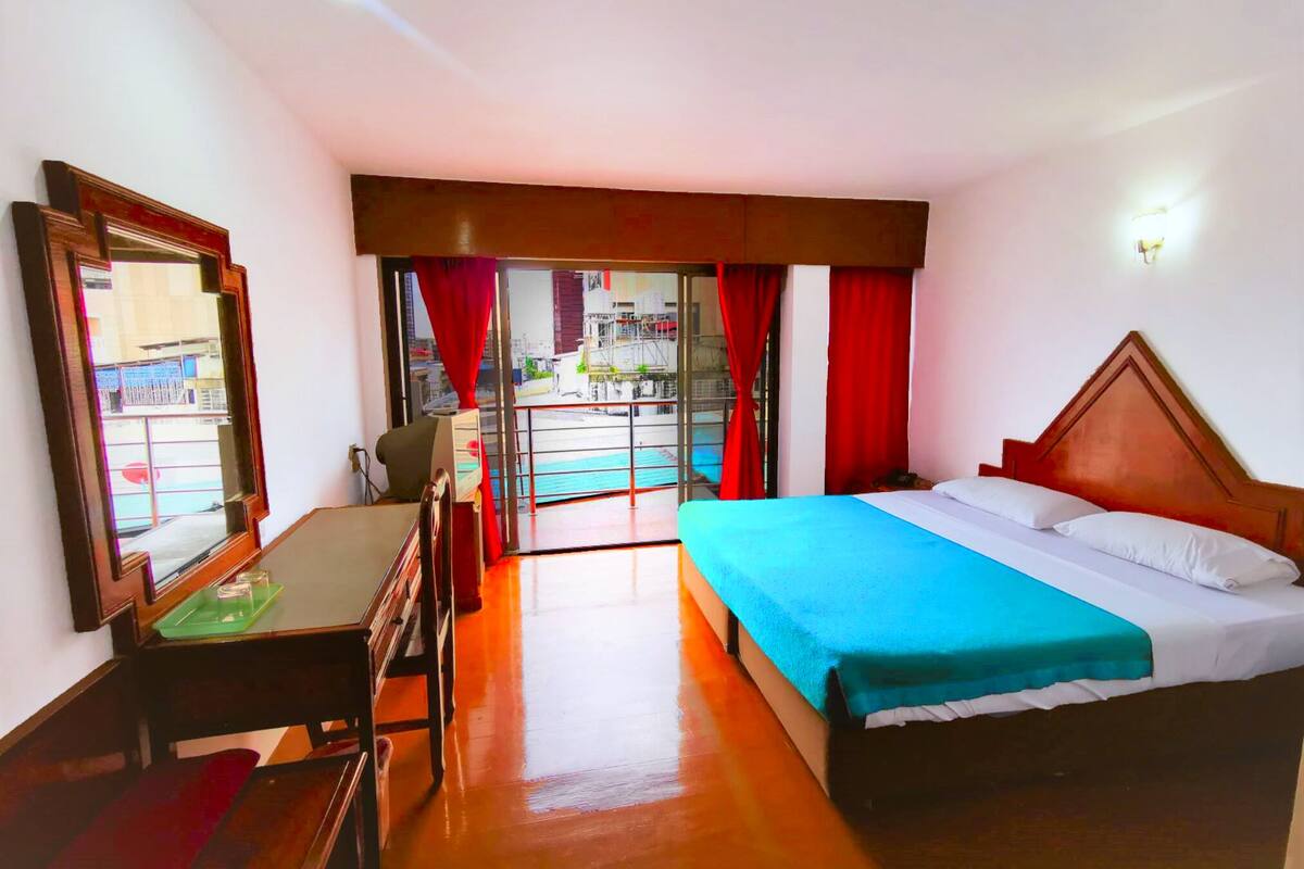 A hotel room with a bed, desk, chair, and a large mirror.